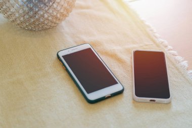 Yemek odasındaki masada cam vazonun yanında masa örtüsü olan iki cep telefonu. Akıllı telefon kavramı.