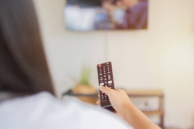 Evde uzaktan kumandalı genç Asyalı kız televizyon izliyor. Arka plan, seçici odak.