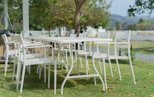 White dining table with chairs in the outdoor garden surround with garden green field. Outdoor dining concept.