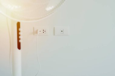 Işık odasında arka fonda elektrik prizi olan modern beyaz bir vantilatör görüntüsü. Fişe seçmeli odaklanma.