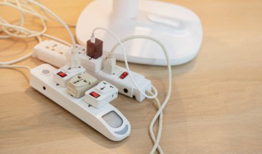 Çeşitli şarj cihazları takılı bir daire zemininde dağınık priz güç uzatma kablosu