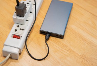 Güç bankasının üst görüntüsü ahşap masada birden fazla soketle şarj ediliyor. Seçici odak.