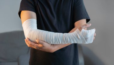 Yaralı kollarına sarılı sargı bezi olan yetişkin bir adamın evde çekilmiş görüntüsü. İlk yardım kavramı.