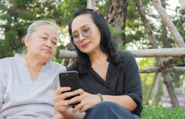 Cep telefonu kullanan mutlu yaşlı kadın ve kız doğa parkında boş zaman aktivitelerinin keyfini çıkarın..