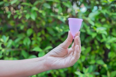 Kadının regl bardağını gerçek doğanın üzerine koyduğu yakın plan görüntüsü. Kadın adeti, adet kupası konsepti..