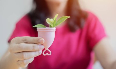 Çiçeklerle dolu pembe regl bardağını tutan kadın, kadın esenliği kavramı. Seçici odak.