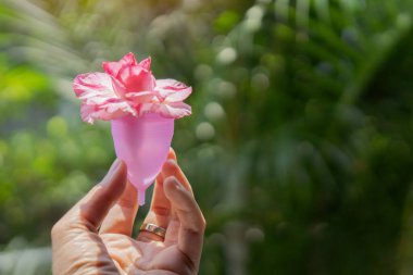 Eko dostu, yumuşak, silikon regl bardağı tutan bir kadın. Çiçeklerle dolu gerçek bir arka plan. Seçici odak, boşluğu kopyala.