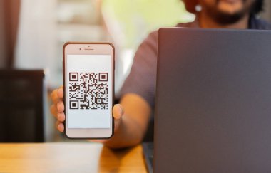 İşadamı telefonu ekranda QR koduyla tutuyor, bilgisayardan sanal ekrana giriş taraması yapıyor. Güvenlik kavramı.