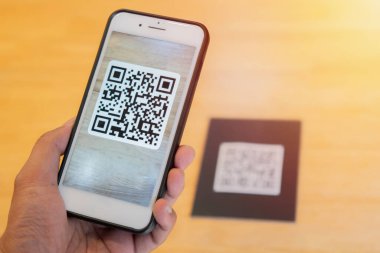 Ekranda QR kodu olan bir cep telefonu tutan bir erkek. QR kodunu tarıyorum. Telefona seçici odaklanma.