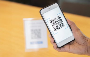 Erkeklerin eli QR kodlarını taramak için bir cep telefonu uygulaması kullanıyor. Masada para ve plastik etiket olmadan dijital ödeme kabul ediyorlar. QR kod ödemesi ve nakit teknolojisi kavramı