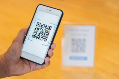 Ahşap masa arkasında cep telefonu ile QR kodu taranıyor. Kod ödemesi, E cüzdanı. Seçici odak.