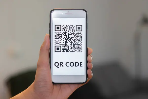 Tanımlanamayan bir adamın eli ekranda QR kodlu modern akıllı telefonu tutuyor. Seçici odak, yakın plan.