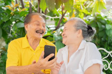 Son sınıf aşığı telefonda uygulamayla video görüşmesi yaparken eğleniyor. Yaşlı Asyalılar dışarıda eğleniyor. Yaşam tarzı kavramı.