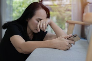 Asyalı olgun orta yaşlı bir kadın evinin yanındaki koltukta oturup kötü haber alınca başarısızlığını kaybettiği için üzülüyor. Seçici odak.