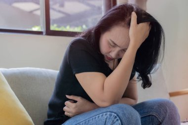 Çekici Asyalı kadın oturma odasındaki kanepede oturup üzgün, yorgun ve endişeli zihinsel sağlık, sorunlar ve kırık kalp konsepti yüzünden depresyon geçiriyor..