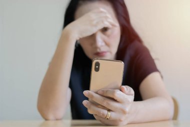 Üzgün kadın akıllı telefonuyla masada oturuyor ve evdeki problemler için endişeleniyor. Seçici odak, boşluğu kopyala.