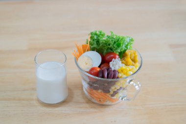 Taze domatesli bir kase meyve salatası, fasulye, arpa pilavı, balkabağı ve yumurta, eski ahşap masada bir bardak süt. Sağlıklı gıda konsepti.