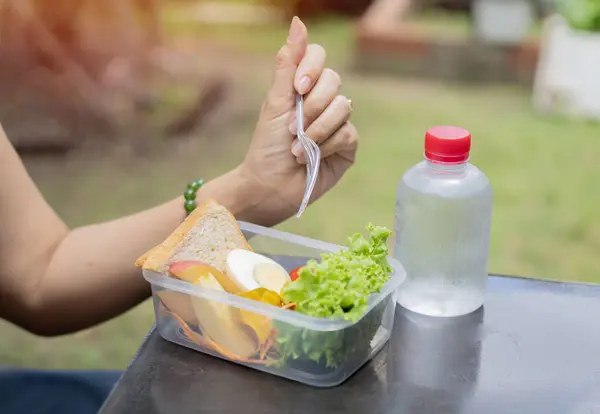 Stock image Side view close up business woman eating salad from her lunch box sitting on the bench at office park.