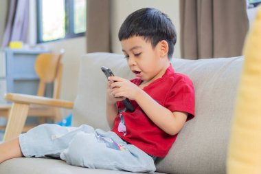 Cep telefonu oyunu oynayan Asyalı çocuk, internetten çizgi film izliyor. Çocuk aleti bağımlılığı. Yan görünüm portresi.