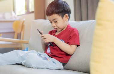 Rahat küçük çocuk cep telefonu kullanıyor, ekrana bakıyor. Akıllı telefonuyla evdeki kanepede oturan sevimli okul çocuğu..