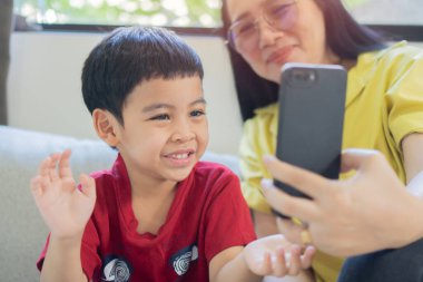 Anneyle küçük çocuğun cep telefonuna bakıp büyükannesiyle görüntülü konuşarak el salladıkları mutluluk. Cep telefonuna seçmeli odaklan.