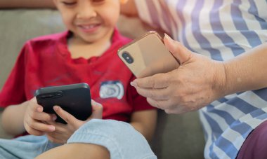 Gülümseyen çocuk ve son sınıf öğrencisi kanepede otururken akıllı telefonla vakit geçiriyorlar. Çevrimiçi oyunlar, sosyal medya. Seçici odak.