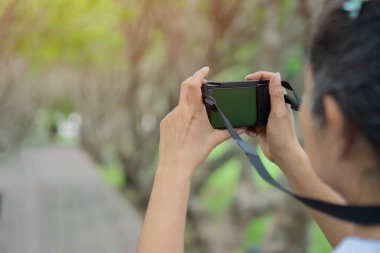 Genç ve neşeli bir kadın yolcunun, doğal parkta dikilirken elinde bir kamera tutuşu. Boşluğu kopyala, seçici odak.
