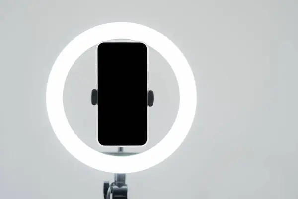 Yüzük ışığı ve beyaz renkli siyah zemin üzerinde siyah ekranlı akıllı telefon olan tripodlar. E-ticaret mesleği konsepti. Boşluğu kopyala.
