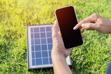 Yakın plan bir adamın elinde, camında güneş paneli olan bir telefon var. Taşınabilir güneş paneli ile cihazları şarj ediyorum. Seyahat için modern teknoloji kavramı