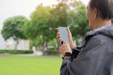 Spor ceketli Asyalı yaşlı sakallı bir adamın gün batımında parkta cep telefonu kullanırken çekilmesi. Boşluğu kopyala.