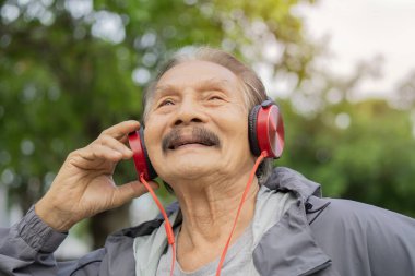 Şehir parkında kulaklıklarıyla tek başına duran gülümseyen son sınıf öğrencisinin fotoğrafı. Rahatlama ve rahatlama kavramı.