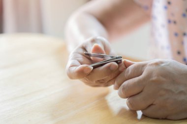 Yakın plan yaşlı kadın, evdeki oturma odasındaki tahta masaya tırnak makası ile tırnak kesiyor. Ev yapımı manikür konsepti.