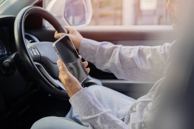 Yaşlı bir adamın cep telefonu kullanırken ya da bakarken arabasını sürüşünün yan görüntüsü. Yolda tehlikeli bir yolculuk.