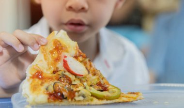 Evdeki yemek odasında pizza yiyen çocuk. Büyük bir pizzanın tadını çıkaran bir çocuğun yakın çekimi. Seçici odak.