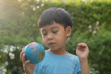 Asyalı çocuğun portresi doğanın arka planında Dünya Gezegeni top oyuncağı oynuyor. Dünya Günü Konsepti.