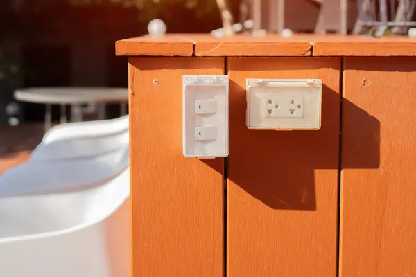 Açık hava beyaz elektrik prizi, parlak kahverengi ahşap duvarla kaplı. Seçici odak.