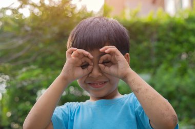 Mutlu gülümseyen Asyalı bir çocuk ve doğal bir geçmişi olan yüzünde işaret eli var. Çocuklar açık hava konsepti oynar..
