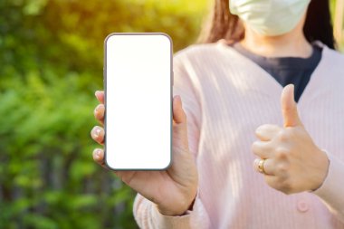 Çevrimiçi servis, teknoloji. Cep telefonunun yakın plan görüntüsü. Ekranı ayırın. Tıbbi maske takan bir kadın tarafından tutuluyor..