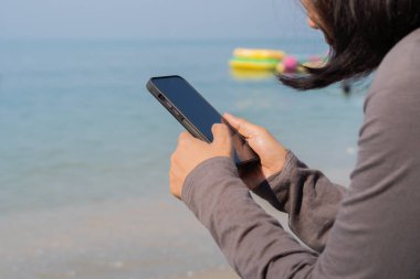 Sahilde bir kadının akıllı telefondan fotokopi uzayıyla mesaj okurken yan görüntüsü..
