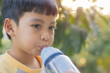 4-5 yaşındaki bir çocuğun portresi. Mutlu Asyalı çocuk, dışarıda fotokopi alanı olan mavi plastik bir şişenin yanında su içiyor..