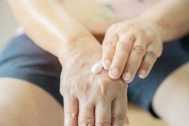 Yaşlı kadın ellerine krem sürüyor. Yakın plan portre. Terapi, güzellik, cilt bakımı. Yaşlanma karşıtı cilt bakımı. Yaşlanma karşıtı cilt kaldırma güzelliği.