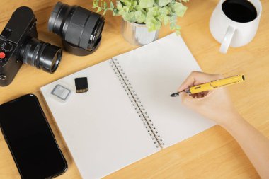 Kameralı, hafıza kartlı, telefonlu ve lensli bir not defterine ahşap masaya yazan biri. Basit yaratıcı çalışma alanı kavramı