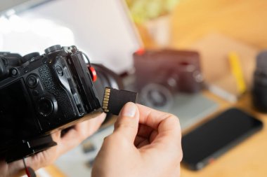 İş yerinde fotoğrafçının elinde hafıza kartı var. Profesyonel DSLR kamerasının yanındaki flaş kart. Yakın çekim, seçici odaklanma.