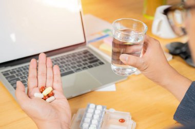 İş adamının arka plan görüşü ve seçici odağı ofiste bir sürü ilaç ve bir bardak su tutuyor. Office Sendromu kavramı.