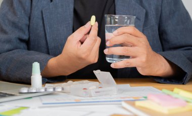 Hasta işçi sağlıksız hissediyor. İş yerinde bir bardak suyla ilaç alıyor. Seçici odak.