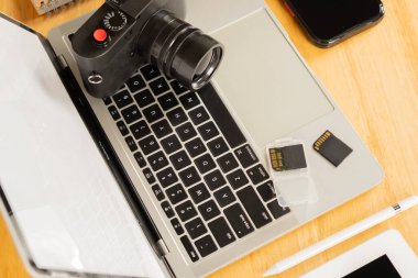 Cep telefonu, dizüstü bilgisayar, z kalemi ve flaş bellekli not defteri ve ahşap bir masanın üzerinde bir kamera. Fotoğrafçının İş Yeri 'ndeki Ögeleri