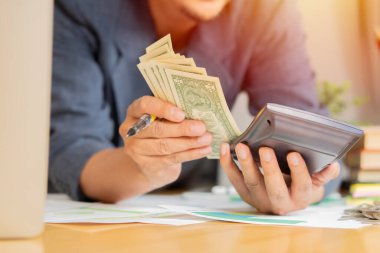 Bir yıl içinde biriktirdiği miktarı hesaplamak için bir hesap makinesi olan bir adam, dolar banknotuyla. Para biriktiriyorum. Finans ve Muhasebe.