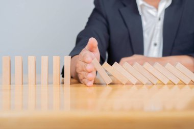 İşadamı domino etkisini eliyle durduruyor. Güvenlik ve sigorta konsepti. Seçici odak.