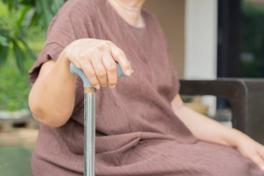 Kıdemli engelli kadın ellerinin baston tutmasını kapatın. Yaşlı kadın dışarıda otururken baston tutuyor. Seçici odak.