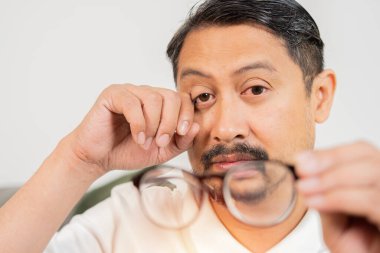 Yetişkin Asain elinde gözlük tutan bir adam gözlerini ovuştururken, yorgun gözlerden muzdarip, göz hastalıkları konsepti. Seçici odak.